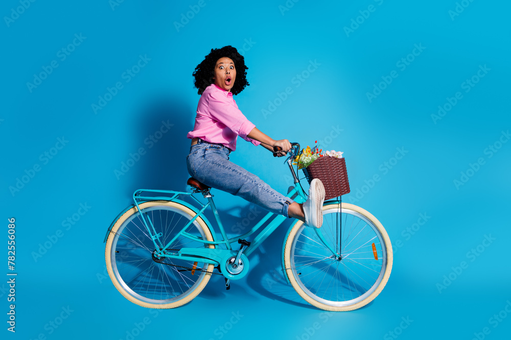 Obraz premium Full length side profile photo of impressed woman wear pink shirt driving bicycle astonished staring isolated on blue color background