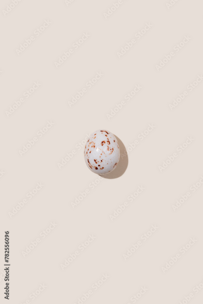 One beige speckled Easter egg casting shadow on beige background, minimalism concept, copy space
