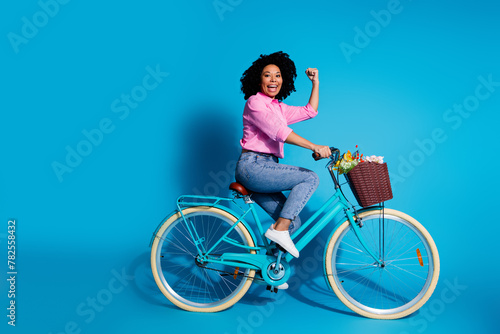 Full length side profile photo of satisfied woman wear pink shirt jeans driving bicycle scream yeah isolated on blue color background © deagreez