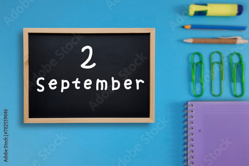 September 2 written in chalk on black board. Calendar date 2st of September on chalkboard on blue blurred school stationery background. Back to school. School event schedule date. Month of autumn. photo