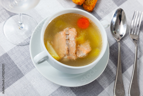 Appetizing rich salmon backbone soup with potatoes and carrots served in white tureen with crispy toasts .. photo