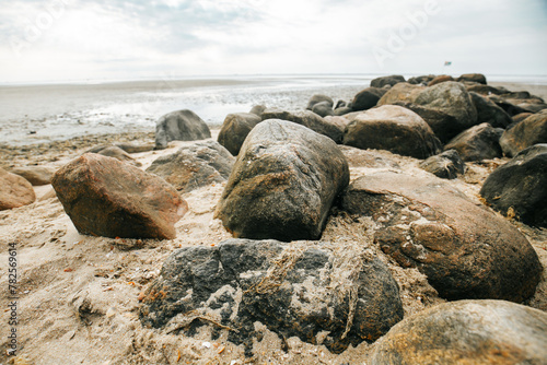 Stone boulders on the beach at low tide.Wadden Sea Coast.Stone groyne close-up on cloudy sky background.. Marine photo wallpaper.Nature of the North Sea coast.  © Yuliya