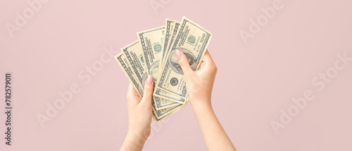 Female hands holding one hundred dollar banknotes on pink background