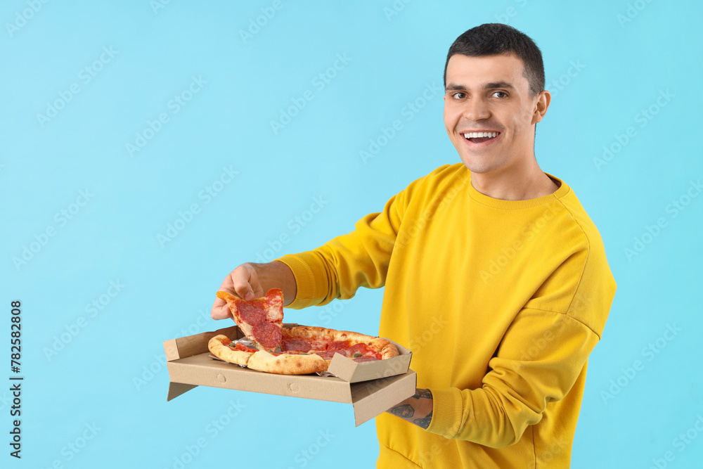 Young man with tasty pepperoni pizza on blue background Young man with tasty pepperoni pizza on blue background