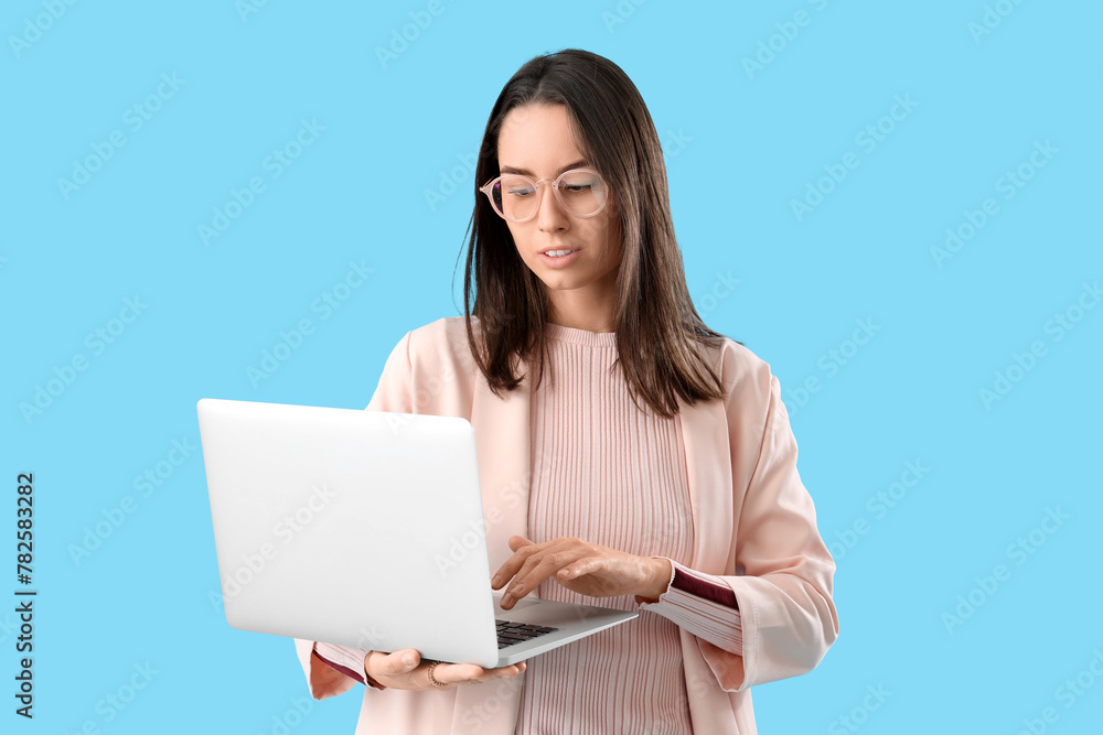 Young woman in eyeglasses using laptop on blue background Young woman in eyeglasses using laptop on blue background