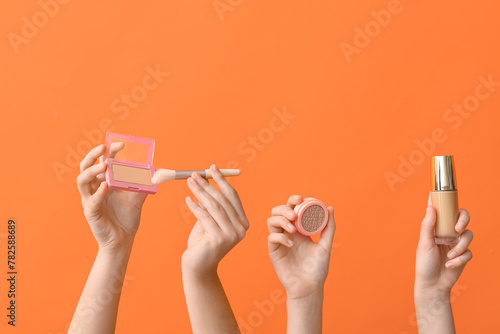 Female hands with powder, brush and foundation on orange background