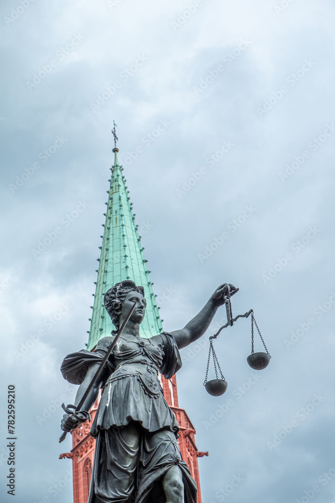statue of lady justice under cloudy sky with church tower statue of lady justice under cloudy sky with church tower