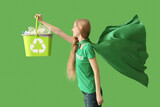Female volunteer in superhero cape holding recycle bin with plastic on green background