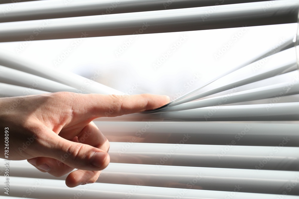 Man separating slats of white blinds indoors, closeup Man separating slats of white blinds indoors, closeup