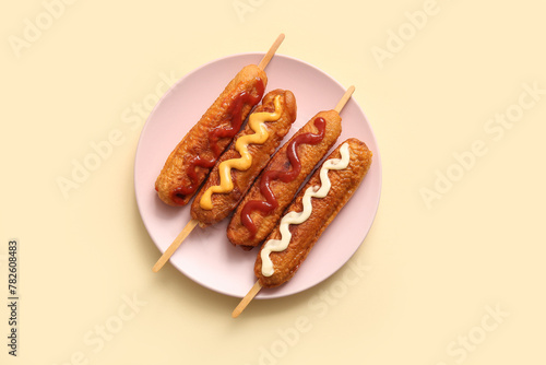 Photography Plate of tasty corn dogs with different sauces on yellow background