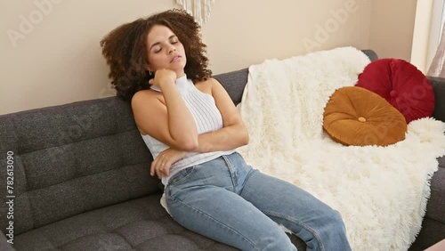 Exhausted hispanic woman with curly hair, bored and sad, mulls over her problems on the living room sofa, crossed arms indicating her depression photo