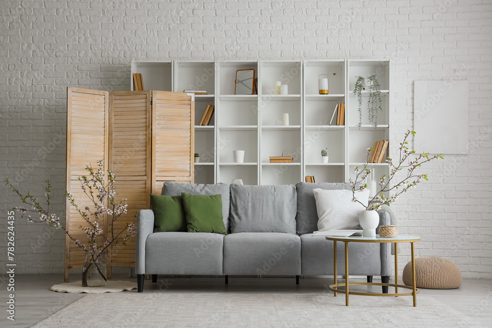 Obraz premium Grey sofa and vase with blooming branches on coffee table in interior of modern living room