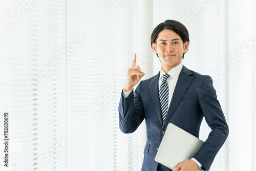 パソコンを持って指差しするスーツ姿の若い男性ビジネスマン（ポイント・誠実・紹介・おすすめ・信頼）
