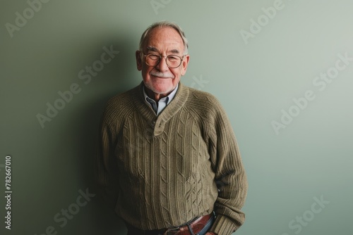 Portrait of a senior man in a sweater standing against a green background.