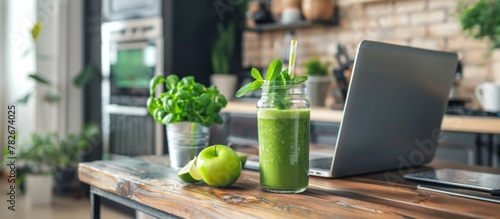 Refreshing green juice in a glass placed beside a modern laptop on a wooden table