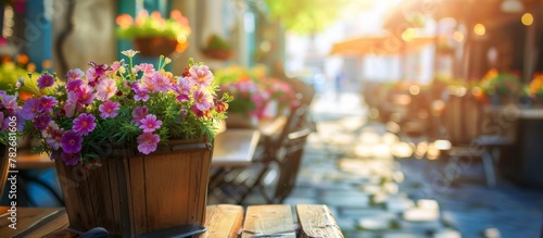 Colorful blooms and greenery arranged in a rustic wooden pot placed outdoors next to a bustling cafe setting