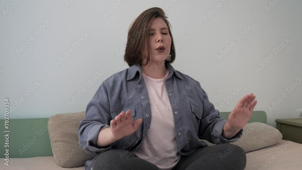 Woman practicing breathing techniques, seated in lotus pose on sofa at home. Woman practicing breathing techniques, seated in lotus pose on sofa at home.