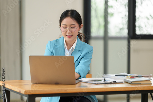 Asian businesswoman wearing glasses smiles Happy working on laptop at office table. Accountant. Online business. Business of finance and marketing financial audit concept.