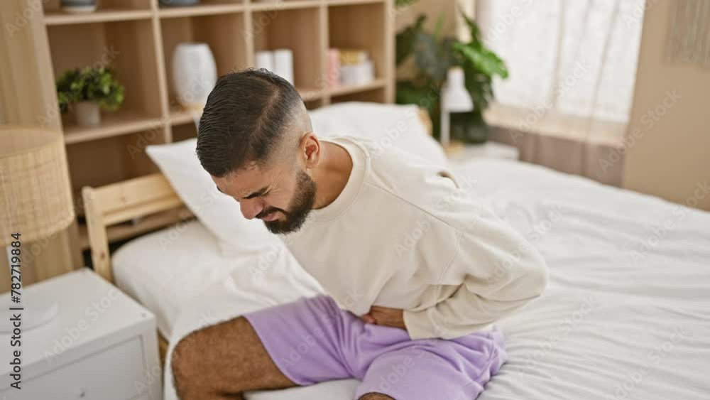A distressed man with a beard feeling stomach pain in a bedroom setting, embodying discomfort and illness. A distressed man with a beard feeling stomach pain in a bedroom setting, embodying discomfort and illness.