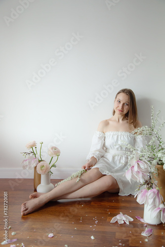 young elegant woman in white dress with spring flowers in vases in white room;