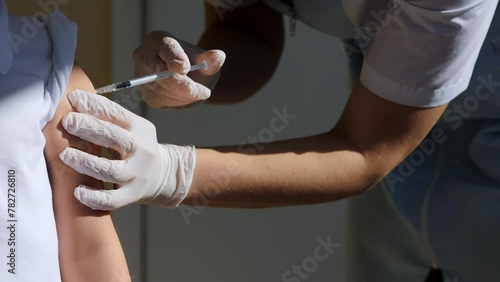 Medical Nurse in Safety Gloves is Making a Vaccine Injection to a child Patient in a Health Clinic. Doctor Uses Hypodermic Needle and a Syringe to Put a Shot of Drug as Treatment. photo