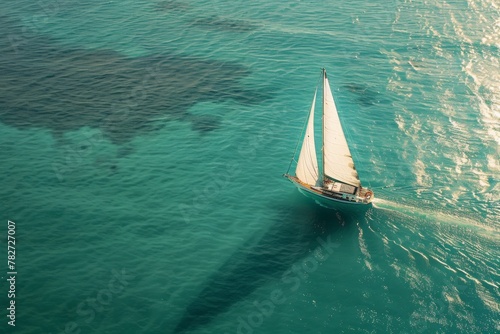 A lone sailboat with billowing white sails, casting a long shadow as it traverses a vast turquoise sea