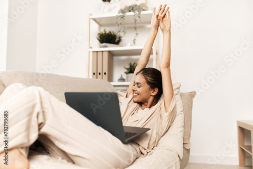 Smiling Woman Working on Laptop in Cozy Living Room, Embracing the Comfort of Modern Technology