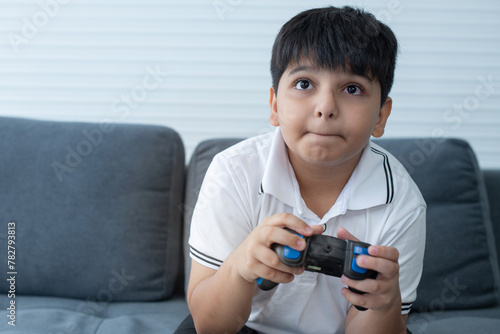 Concentrated Indian boy excited playing video game at home, controlling characters with joystick on couch