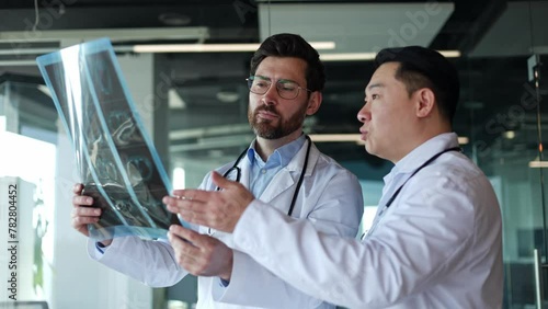 Side view portrait of gentle caucasian and asian males doctors examining x-ray in specially equipped room. Determinative men discussing problem of difficult patient indoors. Concept of diagnosis. photo