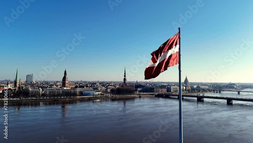 Latvian Flag Waving In The Wind With Bridges Over Daugava River and Riga City In The Background In Latvia. - aerial shot photo