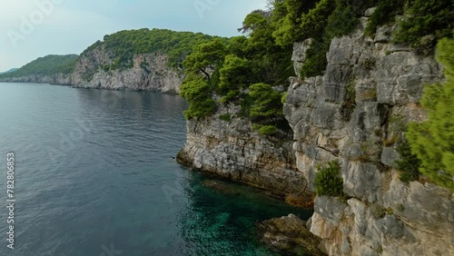 Kalamota Island, Adriatic Sea, Croatia - Clear blue Waters Meet a Rugged Shoreline Beneath Cliffs Covered in Vegetation - Drone Flying Forward photo