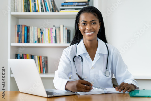 Laughing young latin american female doctor writing notes