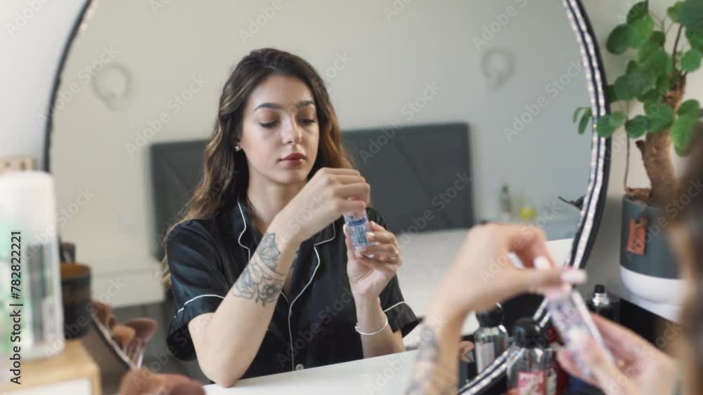 portrait of a young, beautiful woman in pajamas sitting in front of the mirror applying a facial mask portrait of a young, beautiful woman in pajamas sitting in front of the mirror applying a facial mask