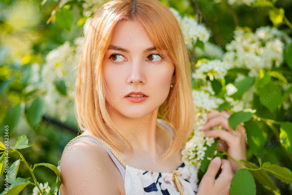 Close-up portrait of an attractive young woman dressed in a dress posing against a background of blooming white apple flowers. Close-up portrait of an attractive young woman dressed in a dress posing against a background of blooming white apple flowers.