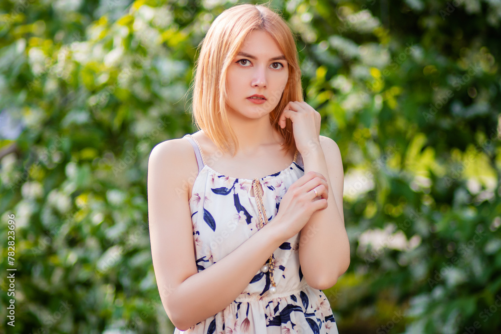 Close-up portrait of an attractive young woman dressed in a dress posing against a background of blooming white apple flowers. Close-up portrait of an attractive young woman dressed in a dress posing against a background of blooming white apple flowers.