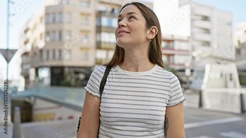 Contemplative young woman with long brunette hair on urban city street, outdoors. photo