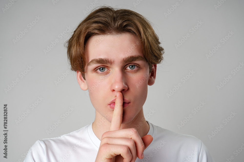 Young Man With Finger on Lips Signaling Silence Against a Plain Background Young Man With Finger on Lips Signaling Silence Against a Plain Background