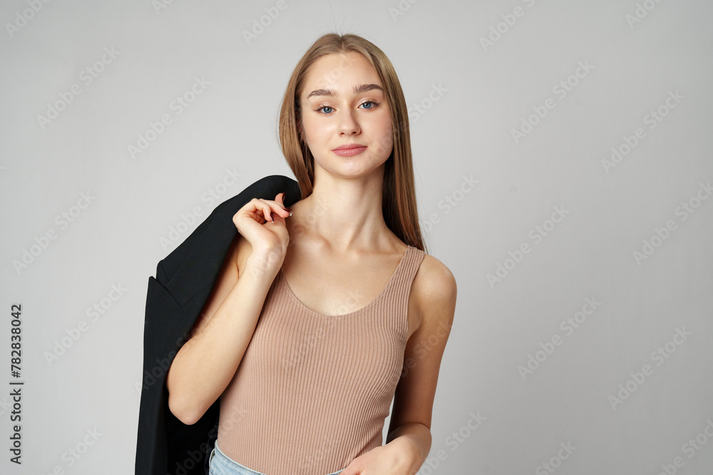 Young Woman in Casual Blazer and Jeans Smiling Against a Grey Background