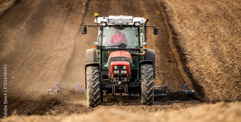 Fototapeta premium Powerful tractor with plow in action, turning the rich soil for new crops
