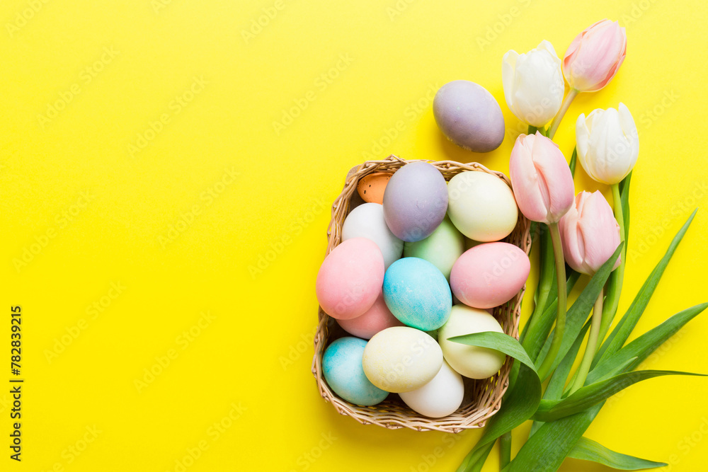 Happy Easter composition. Easter eggs in basket on colored table with yellow Tulips. Natural dyed colorful eggs background top view with copy space Happy Easter composition. Easter eggs in basket on colored table with yellow Tulips. Natural dyed colorful eggs background top view with copy space