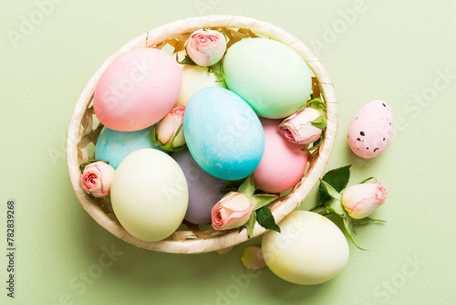 Happy Easter. Easter eggs in basket on colored table with yellow roses. Natural dyed colorful eggs background top view with copy space