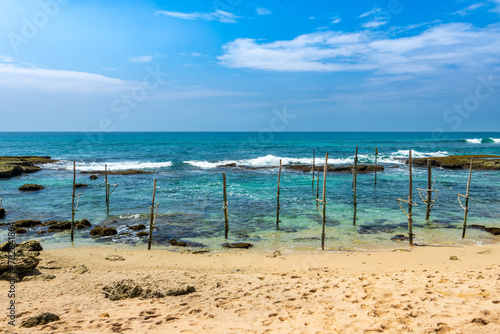 Stunning coastal scene with blue skies  coconut trees  and a thatched hut. Traditional stilt fishing adds to the charm. Southwest Coast  Sri Lanka.