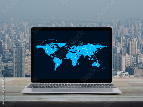 Connection line with global world map on laptop computer monitor screen on wooden table over city tower and skyscraper, Business communication online concept, Elements of this image furnished by NASA