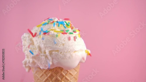 wafer cone with scoop of ice cream covered and strewing sprinkles on pink background, copy space, super slow motion, close up