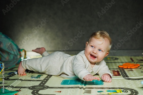 A 7-month-old baby is lying on a rug and playing. The child holds his head. A baby learns to crawl on the floor. A child in a beige romper.