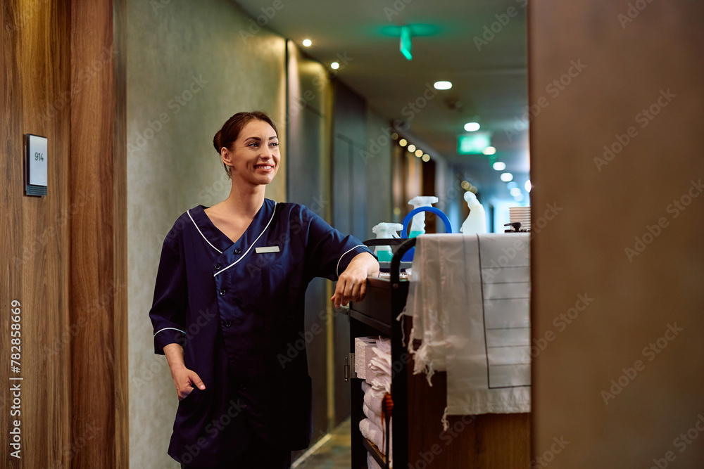 Smiling hotel housekeeper with chambermaid's trolley in hallway. Smiling hotel housekeeper with chambermaid's trolley in hallway.