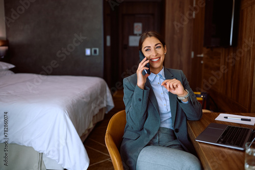 Happy entrepreneur talking on cell phone from hotel room during her business trip.