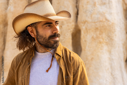 A man wearing a cowboy hat and a brown shirt is standing in front of a wall. He has a beard and a mustache photo