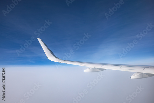 Airplane flying above snowy mountains landscape on a sunny day, view from plane window of clouds and wing turbines