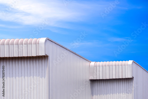 Two modern metal industrial warehouse buildings with aluminium roof eaves against blue sky background, perspective side view with copy space 